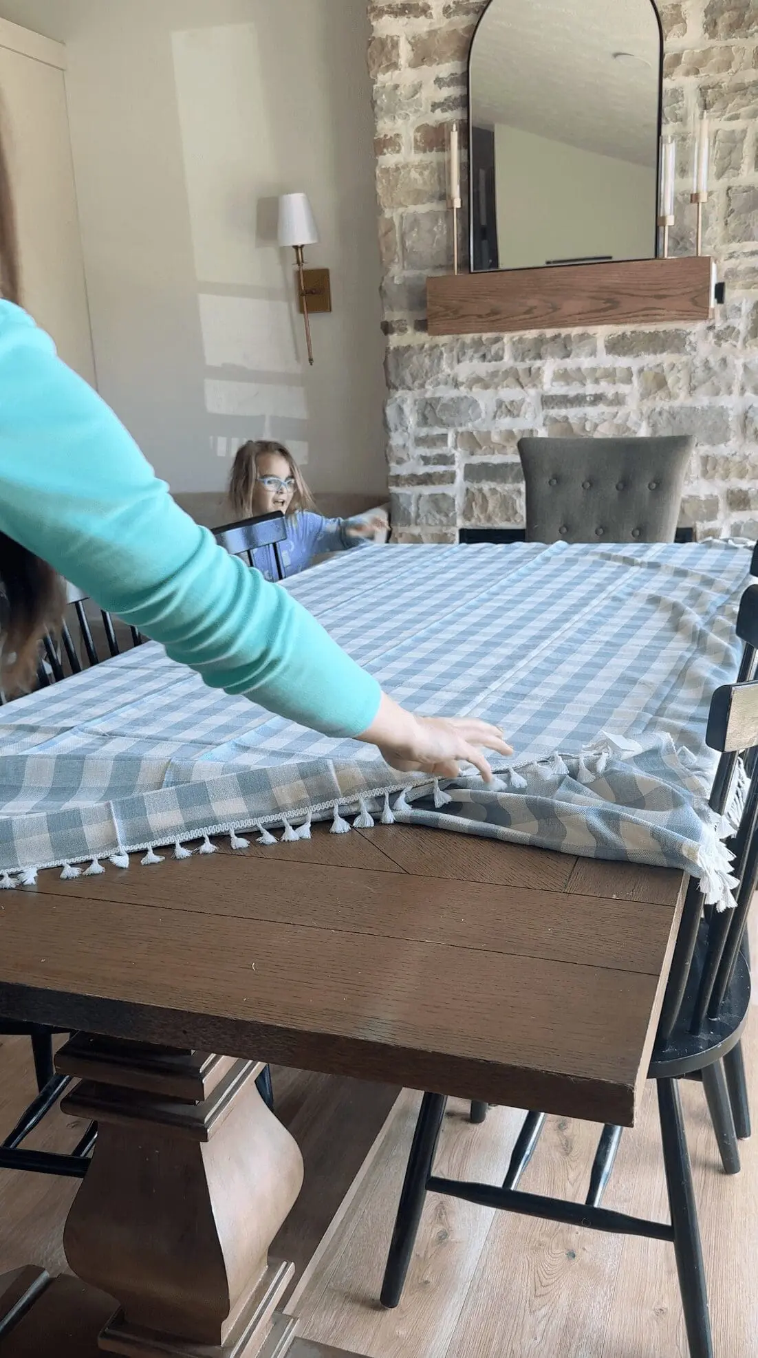 Woman and child setting a blue gingham tablecloth with tassel trim.